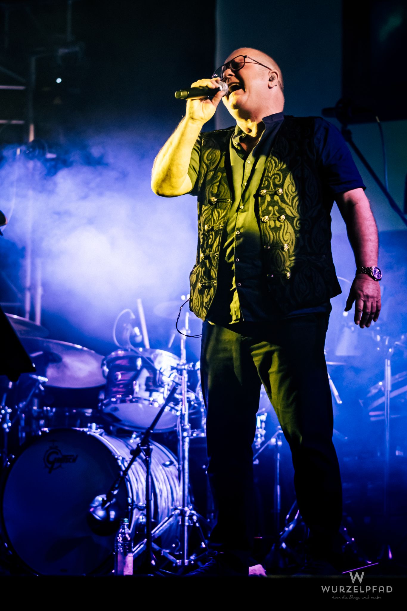 Sänger von Beyond – A Pink Floyd Tribute live auf der Bühne. Der Musiker singt leidenschaftlich ins Mikrofon, umgeben von intensiven blauen und gelben Bühnenlichtern und atmosphärischem Rauch.